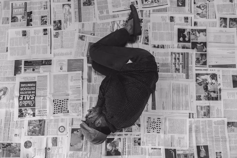 Man laying on news papers hiding his face, conceptual digital photography, 'Linji Sfużi' - a collection of short stories and photography