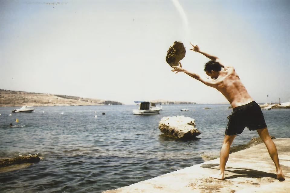 Man throwing a boulder into the sea, summer time in Malta