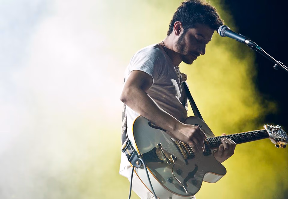 Frontman and singer, mid-performance, green and yellow stage light, Airport Impressions, Beland Festival Malta